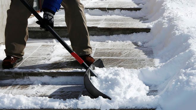 Worker clearing snow from driveway and sidewalk with shovel for safe winter property access